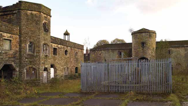 The courtyard of a derelict 16th century manor house. It is covered in overgrown grass and shrubbery.