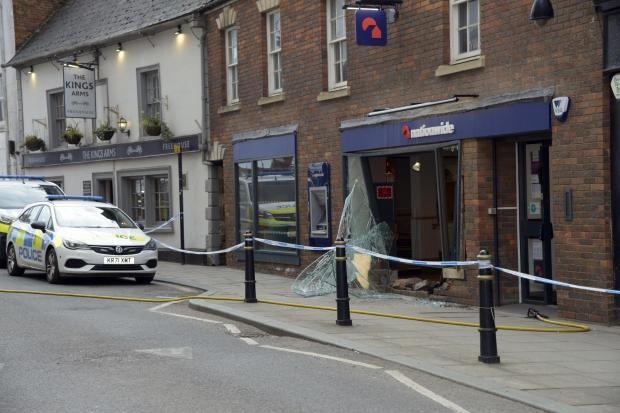 A cordon up on Castle Street, showing the front of the bank branch smashed by the car. Mangled glass is hanging out the storefront, and bricks are strewn on the ground. 