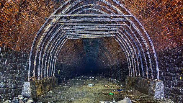 A red-bricked railway tunnel lined with some grey metal tubing.