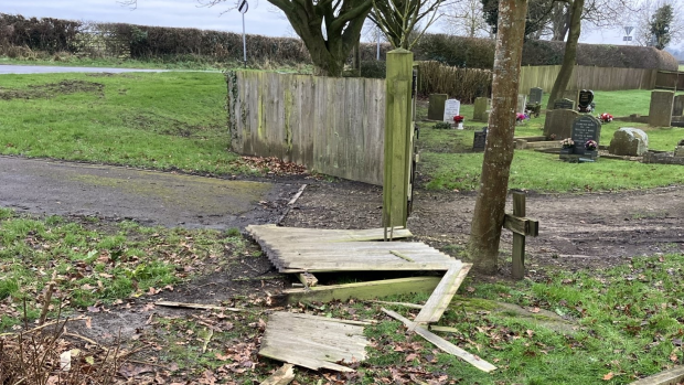 A smashed fence in front of some gravestones