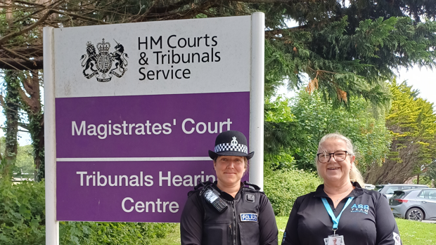 Sgt Alice McKinnon (left) and Kay Smith, anti-social behaviour officer for Camborne at Cornwall Council, stand next to a purple and white sign for Truro Magistrates' Court.