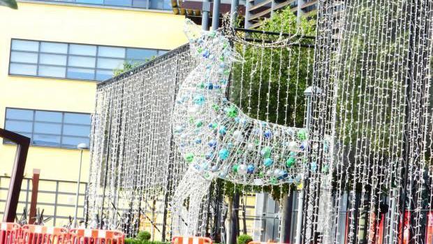 A large reindeer Christmas decoration covered in lights and baulballs is outside a pale yellow building at West Herts College. There is a curtain of Christmas lights either side