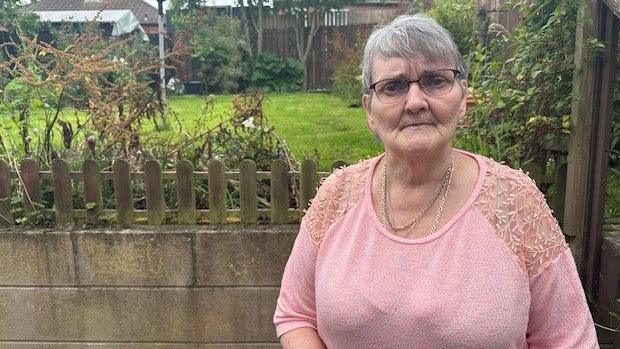 Woman with grey hair and black glasses in pink top