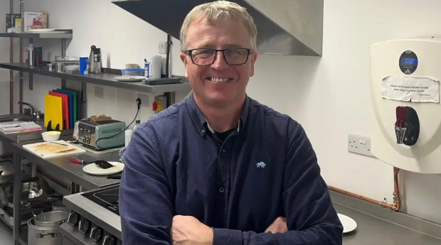 Man in blue shirt stood in a kitchen setting