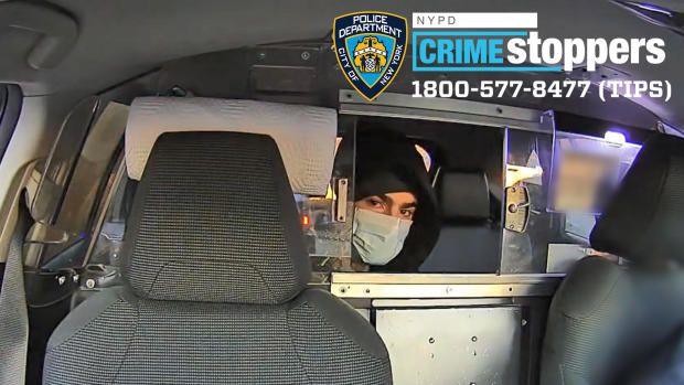 A hooded man wearing a face mask sits in the back of a vehicle looking through a dividing window