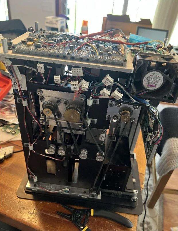 The inside of a rigged card-shuffling machine shows wires and mechanisms. It is sitting on a desk