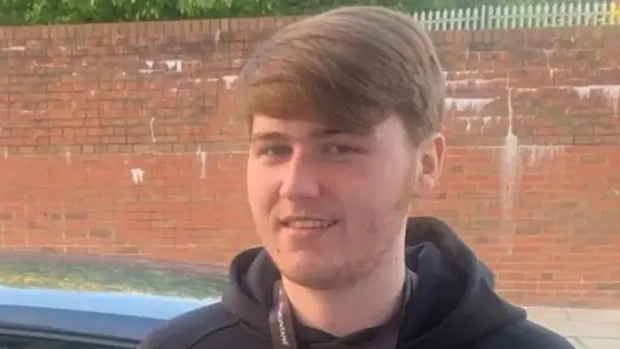 A family handout of Ellis Cox. He has short brown hair and is wearing a dark hoodie. He is standing in front of a red brick wall.