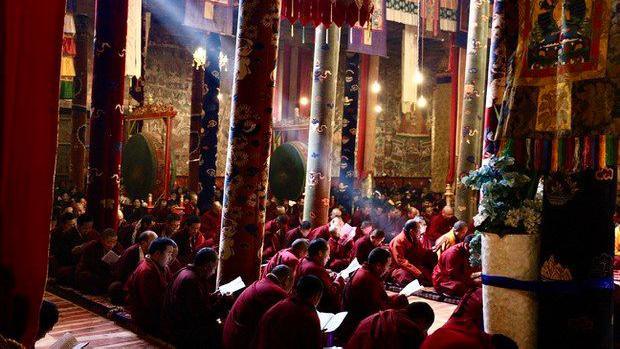 A photo showing seated red-robed monks praying inside the Wontoe Monastery in Dege county. 