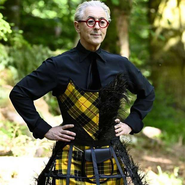 A snap from Traitors USA of Alan Cumming in a black shirt and a yellow and black tartan kilt and bustier.