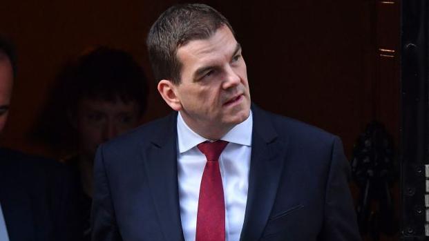 Oliver Robbins looks away from photographers as he exits 10 Downing Street wearing a suit during his time as Brexit negotiator in 2019