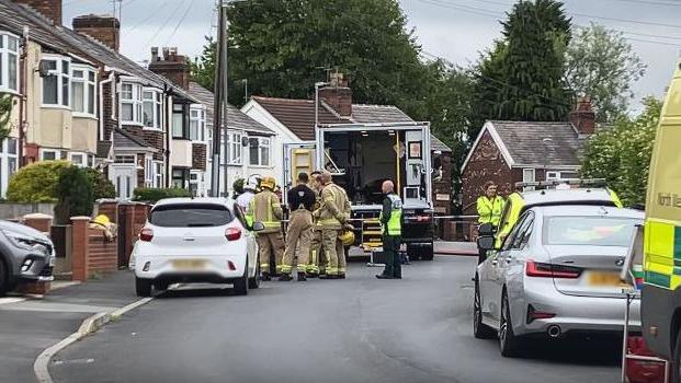 Emergency services in a residential street gathered in front of emergency vehicles - in between residents' parked cars - as they deal with the discovery of explosives in a home in St Helens.
