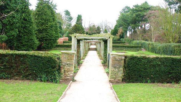 Part of West Bank Park, with hedges and a wood-framed tunnel, surrounded by grass and trees