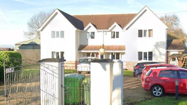 A whitewashed building with metal gates in front of it. There a four cars parked in the driveway