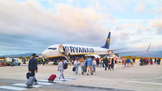 Passengers line up to board a Ryanair aircraft on an airport runway under a colourful sunset sky. 