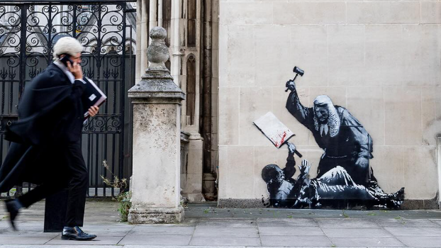 A member of the legal profession walking past a Banksy mural on the walls of the Royal Courts of Justice