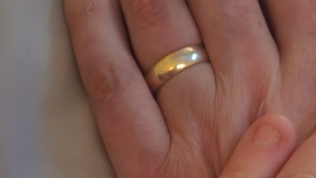 A gold band is worn on the wedding finger of a man's hand which is shown in closeup.