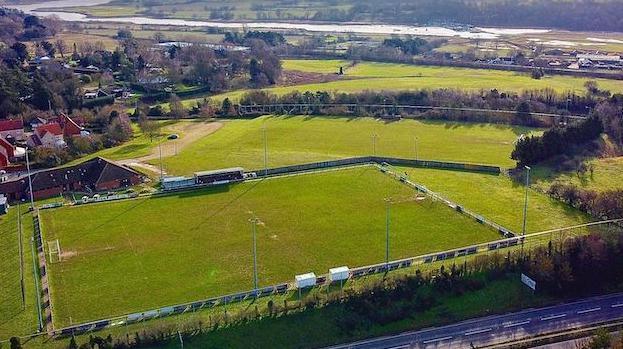 An aerial shot of Woodbridge Town FC. It shows the ground which has tall pitch lights at its corner and a small stadium on its far side