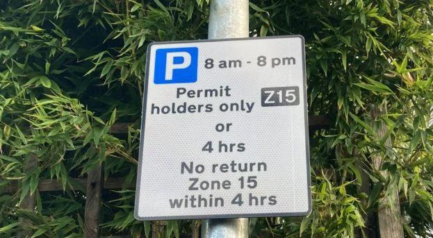 A sign that reads "Parking 8am-8pm, permit holders only or 4 hours no return zone 15 within 4 hours"