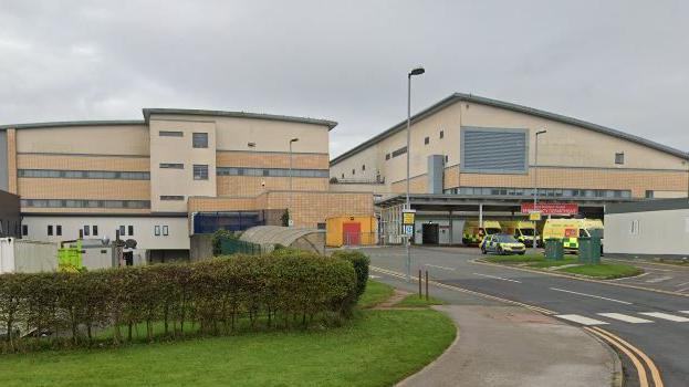 A street view of the exterior of the A&E department, where liveried ambulances are parked outside the entrance.