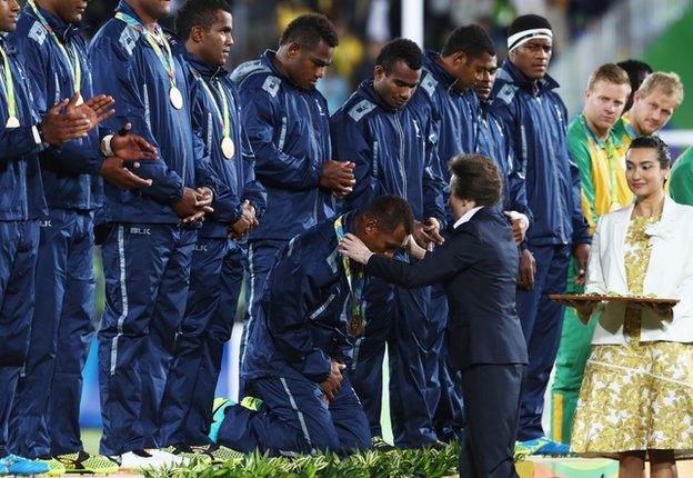 The Fiji players, renowned for both their humility and size, kneel to receive their medals from the Princess Royal