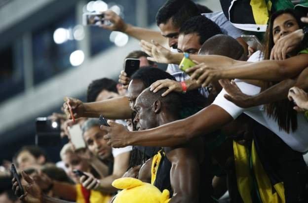 Usain Bolt in a crowd taking selfies.