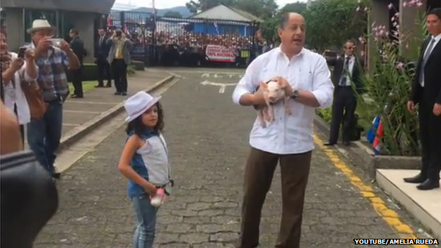 President Solis holding the piglet while standing next to the young girl who handed it to him