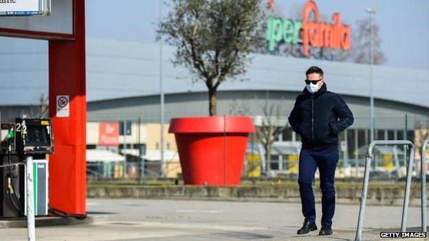 A man wearing a surgical mask walks along a deserted street in the Italian town of Codogno