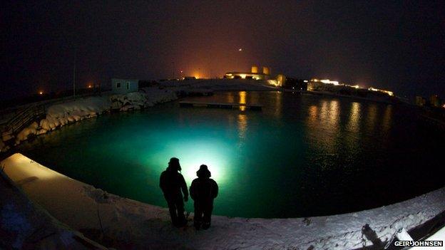 Two people stand by a turquoise blue pool