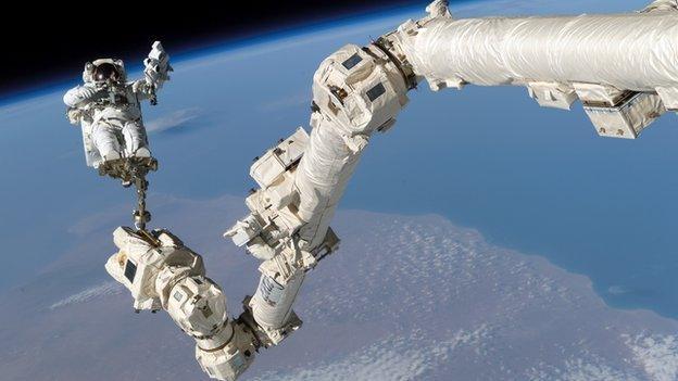 A spacewalking astronaut attached to a robotic arm