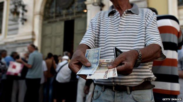 A pensioner holds banknotes next to people waiting outside a national Bank branch as banks only opened for pensioners to allow them to cash out up to 120 euros, in Athens on July 1, 2015.