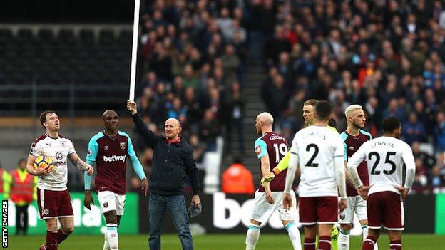 A supporter holds a corner flag after coming onto the pitch