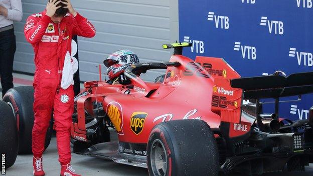 Charles Leclerc holds his head in his hands in the parc ferme after the race