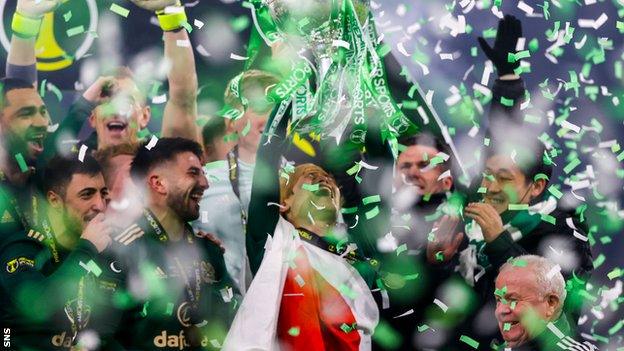 Kyogo Furuhashi, draped in a Japan flag, lifts his first Celtic trophy after his match-winning show in the final