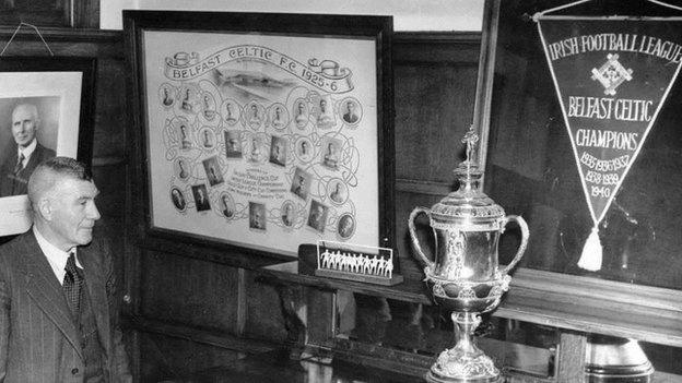 Belfast Celtic manager Elisha Scott looks proudly at the silverware in the club boardroom