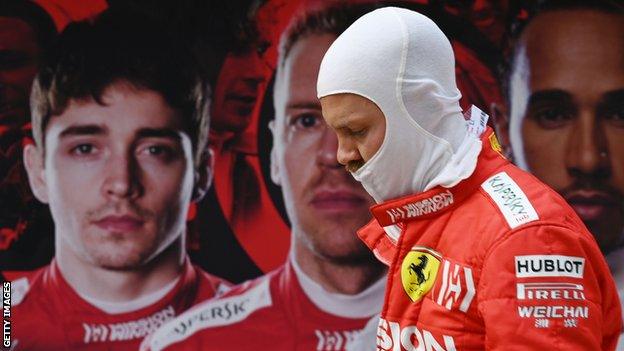 Sebastian Vettel walks past a poster of team-mate Charles Leclerc, Vettel and Lewis Hamilton