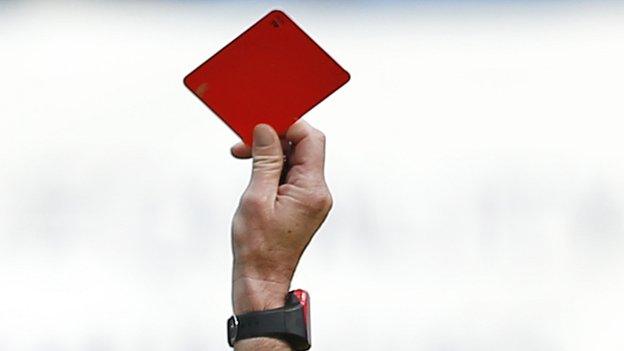 A football referee brandishes a red card