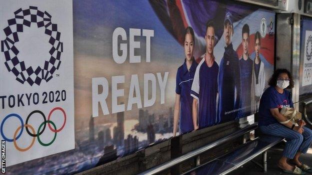 Woman wearing a mask at a bus stop with Tokyo 2020 advertising