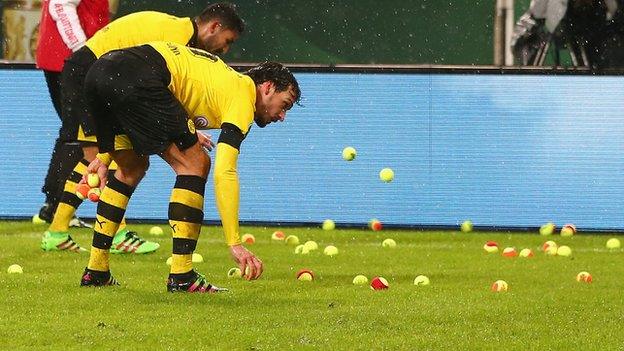 Dortmund players attempt to clear the pitch of tennis balls