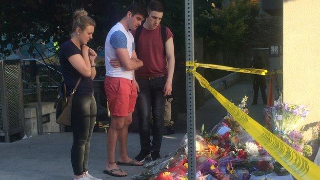 People look at flowers and photos at the scene of the accident