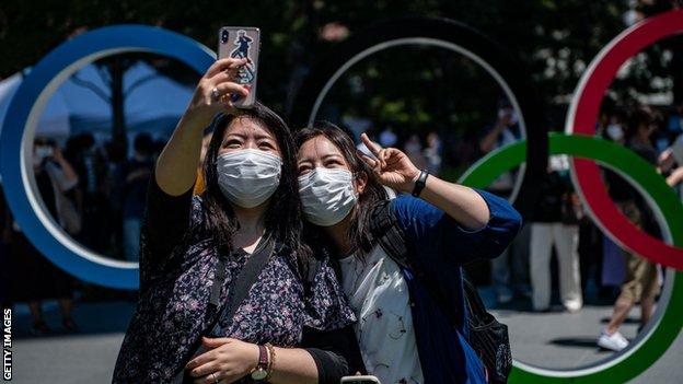 Japanese women pose for a selfie by the Olympic rings