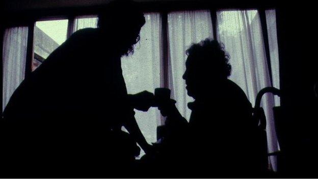 Silhouette of elderly woman being given tea by carer