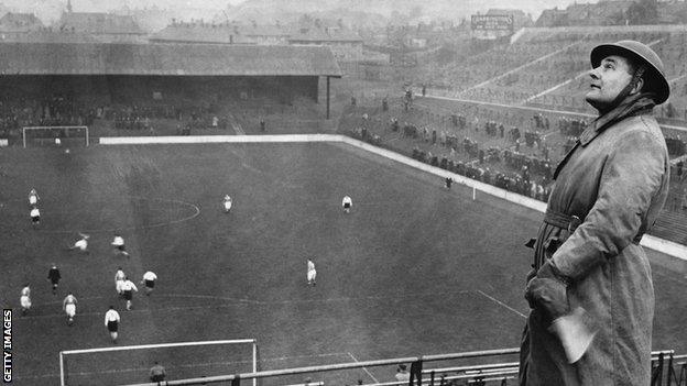 An air raid warden on the look-out for enemy planes at a football match between Charlton and Arsenal, 1940