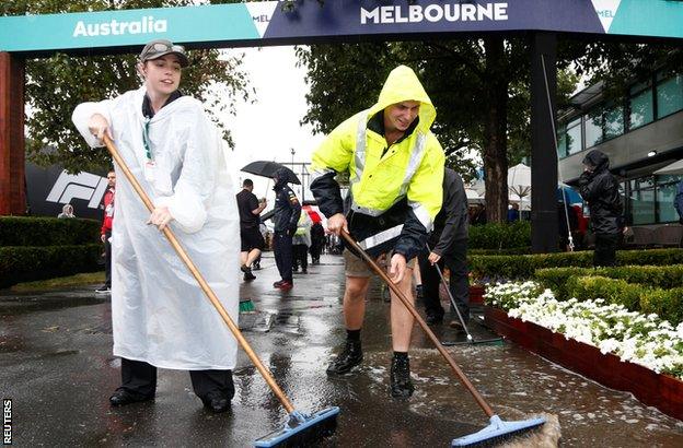 Workers clear water from the paddock before practice