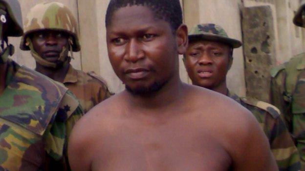 Mohammed Yusuf, bare-chested and with a bandage on his arm, surrounded by soldiers