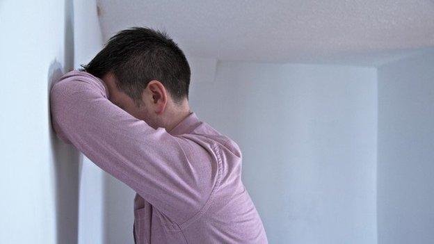 Man leans on wall with his face resting on his arm