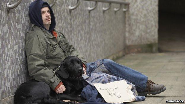 A man with a dog begging next to an underpass, holding a sign that says 'homeless and hungry'