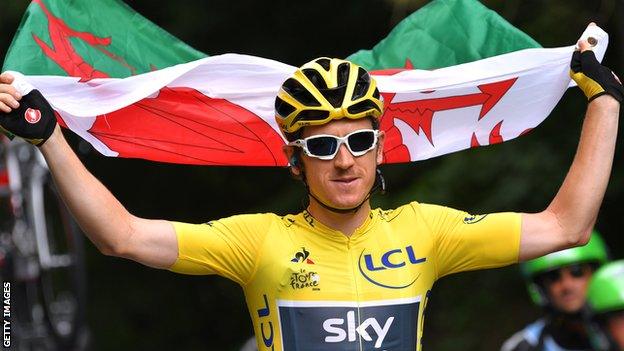 Geraint Thomas hold the Wales flag aloft while wearing the yellow jersey in celebration after winning the 2018 Tour de France