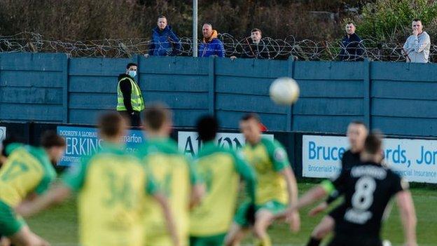 Cefnogwyr Caernarfon yn gwylio'u tîm yn herio Cei Connah tu hwnt i'r wal sy'n amgylchynu'r Oval