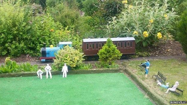 A model train passes figures playing bowls at Bondville