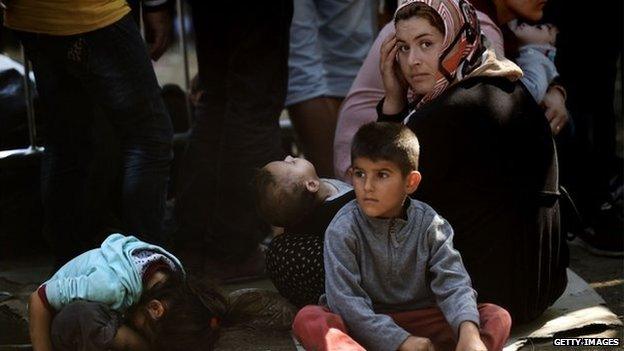 Syrian refugees and migrants wait with children at a registration camp in Presevo after their arrival in Serbia on 30 August 2015